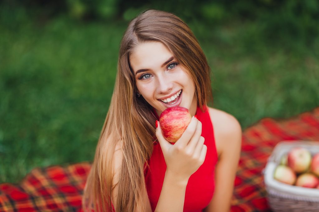 A woman smiling while holding an apple as a symbol of a dental-friendly fruit