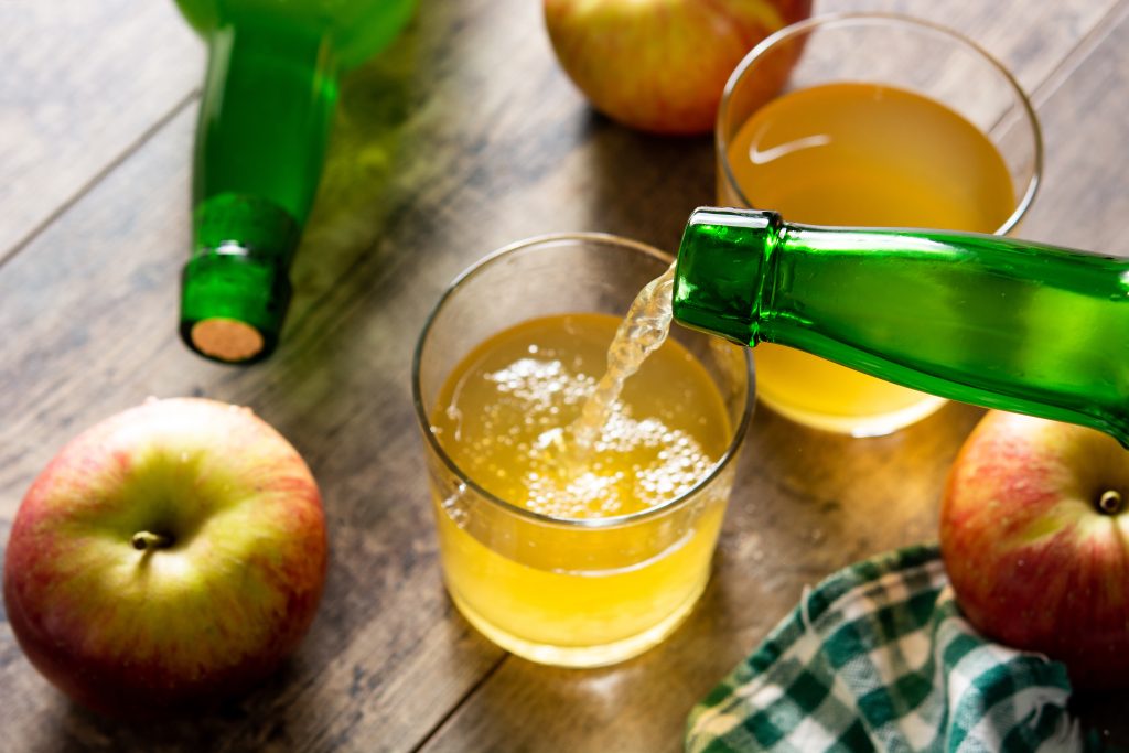 Apple juice is being poured into a clear glass mug, emphasizing freshness.