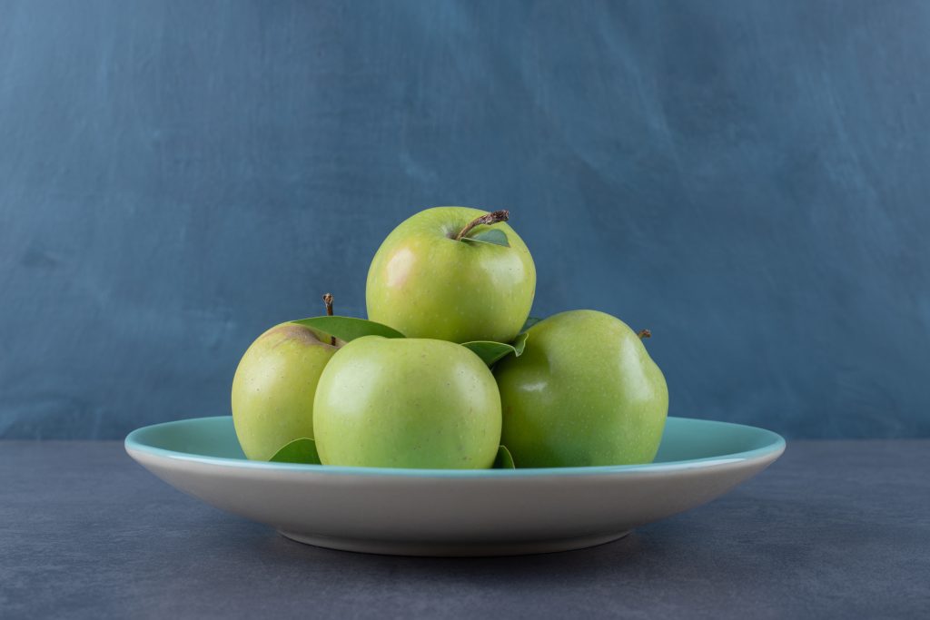 green apple on plate over grey background.