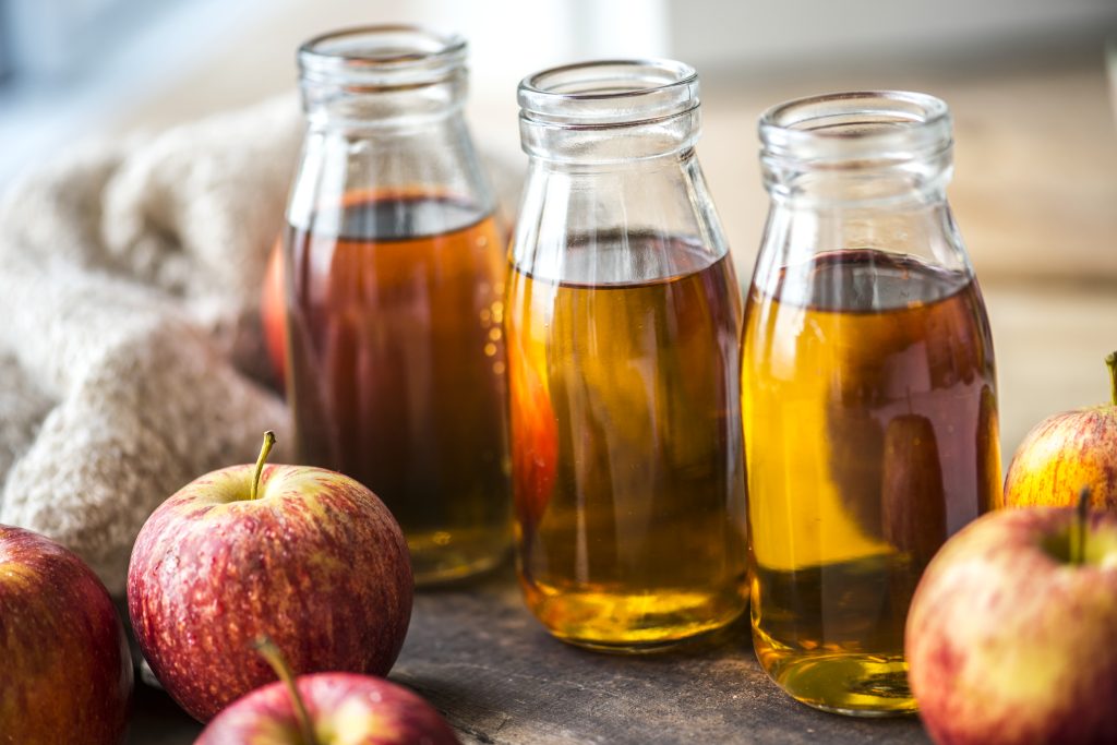 fresh apple cider with whole apples on a wooden table, showing freshness