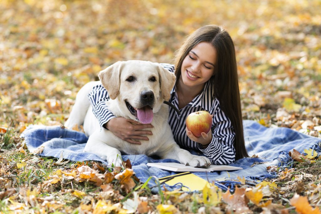 happy woman holding her white puppy and sharing an apple with the dog
