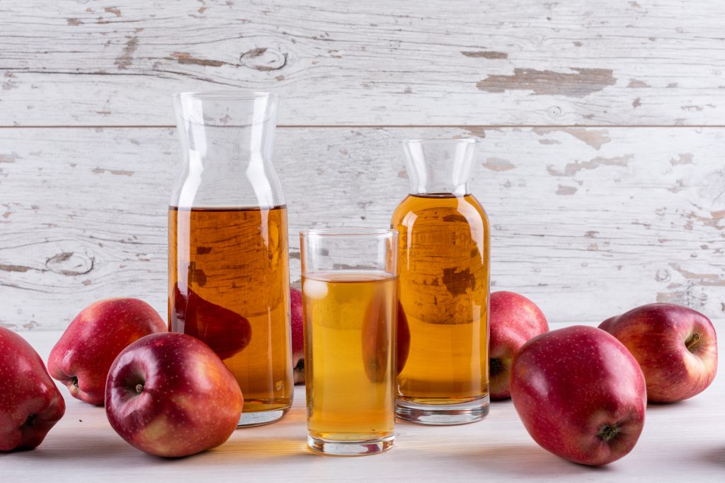 Apple cider with red apples on a white wooden table.