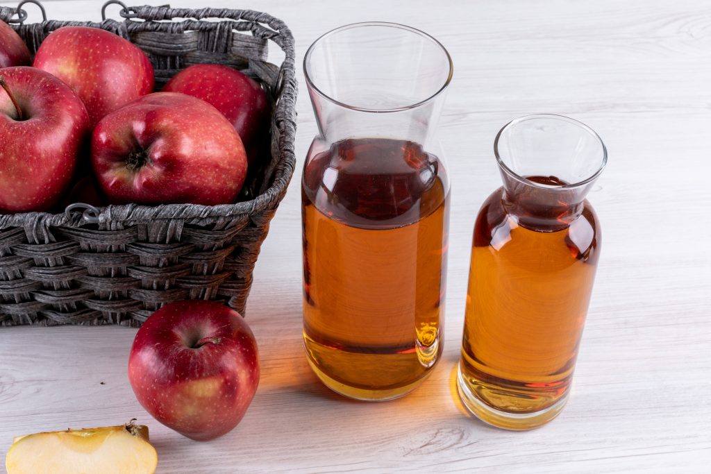 red apples in a basket with apple cider vinegar on a white wooden table