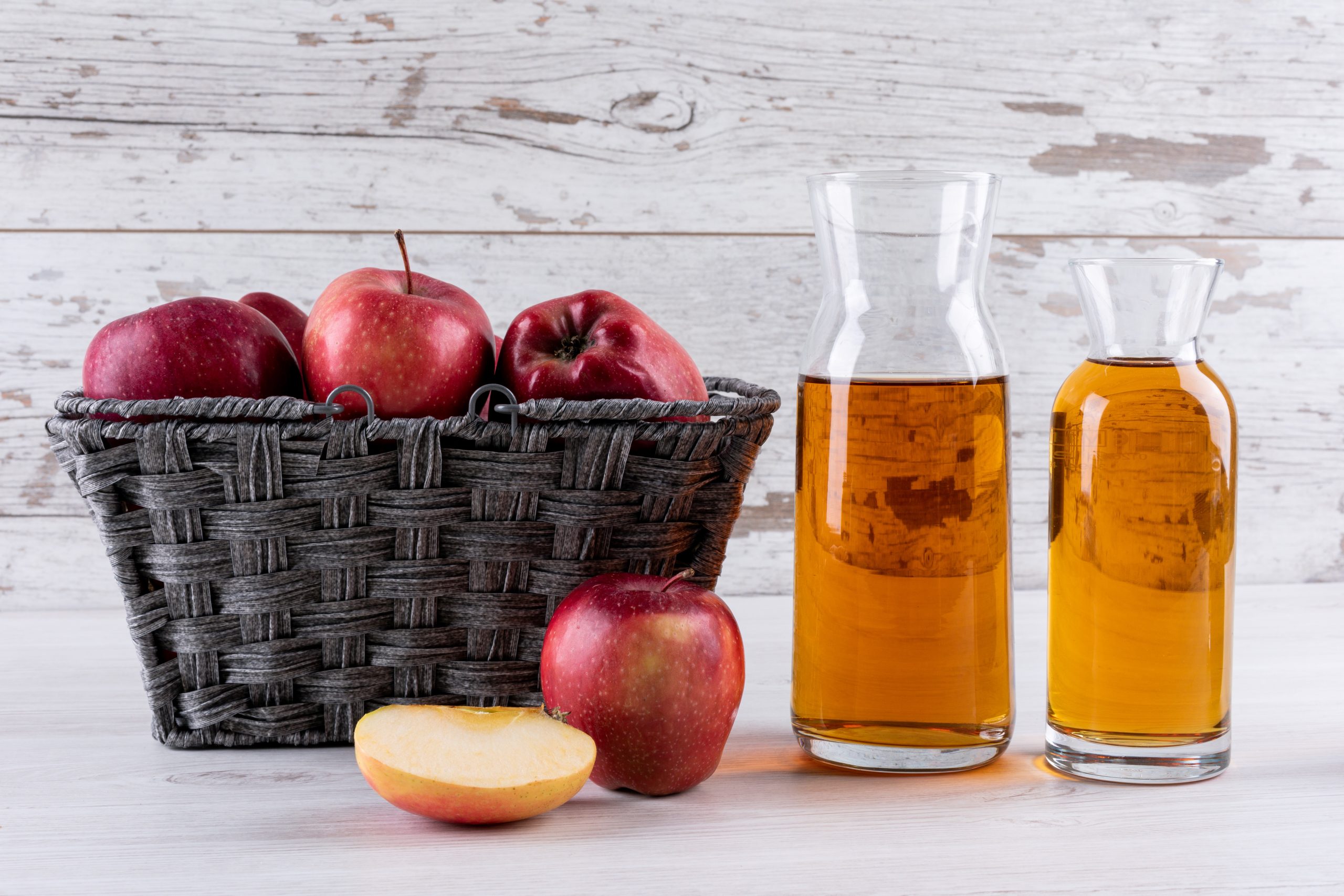 side view red apples basket with juice, on white wooden table