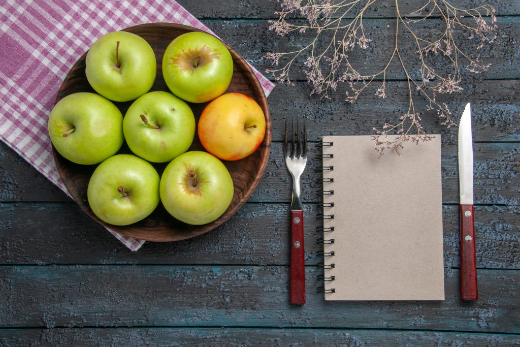 Green and yellow apples in a plate with a notebook and fork showing nutrients and iron benefits in it