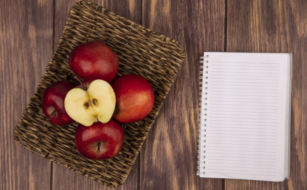 fresh juicy and red apples on a wicker tray on a wooden background with notebook