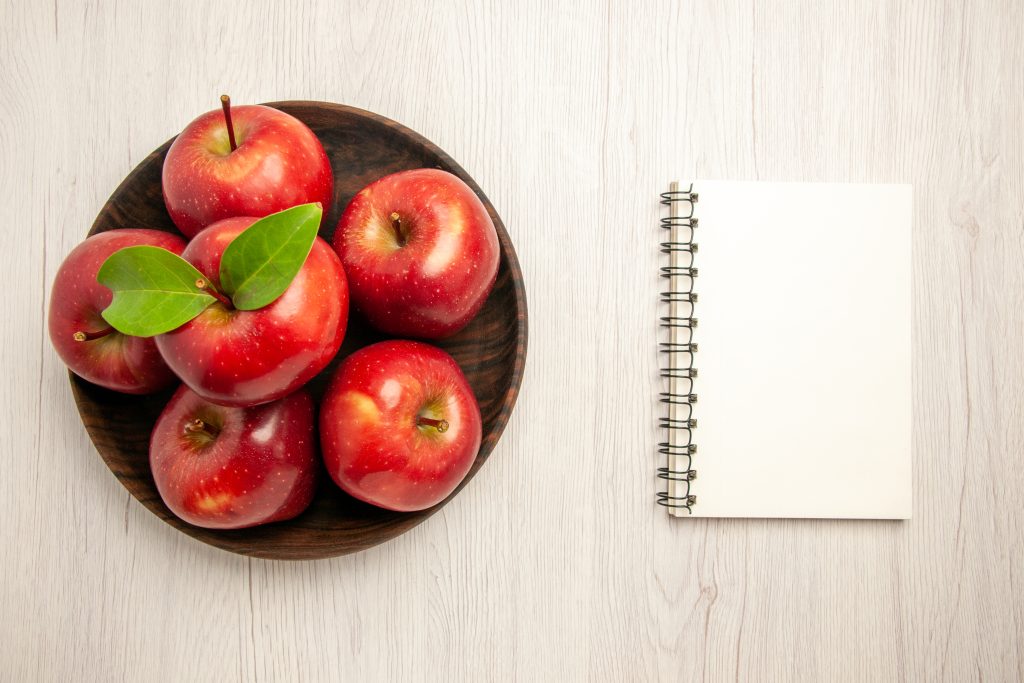 Fresh red apples on a white wooden table with notebook